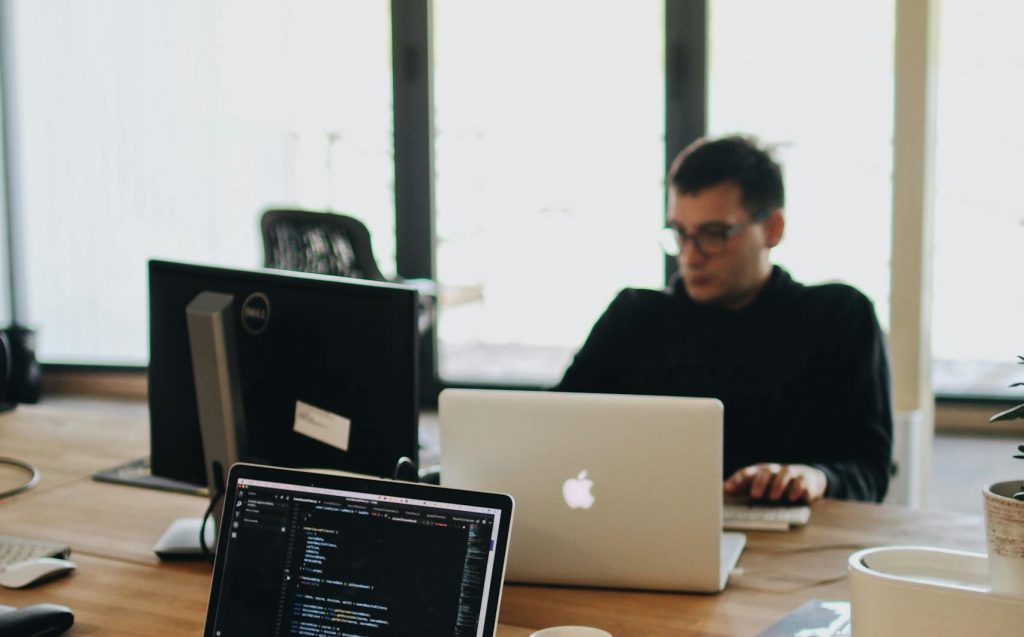 A web developer working on code in a modern office setting with multiple devices.